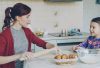 Young mother rolling dough and talking to her little cute daughter while cooking in the kitchen on weekend. Family, food, home and people concept